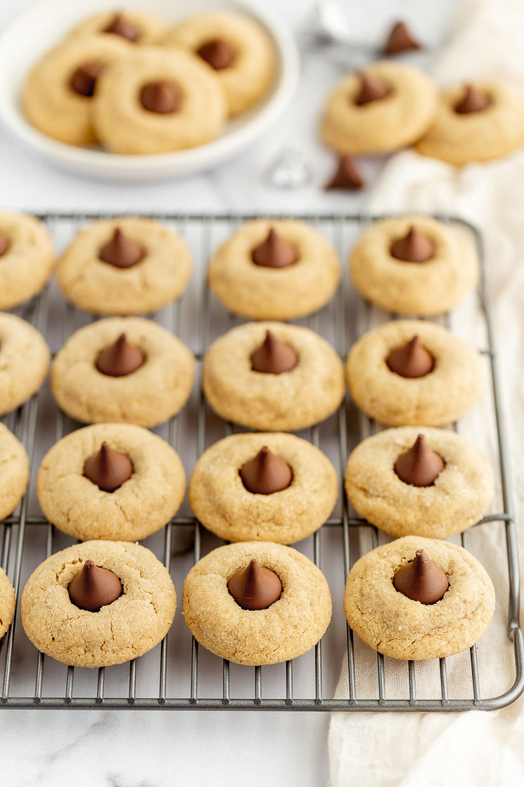 A cooling rack holding peanut butter blossoms with more in the background on a plate and napkin.