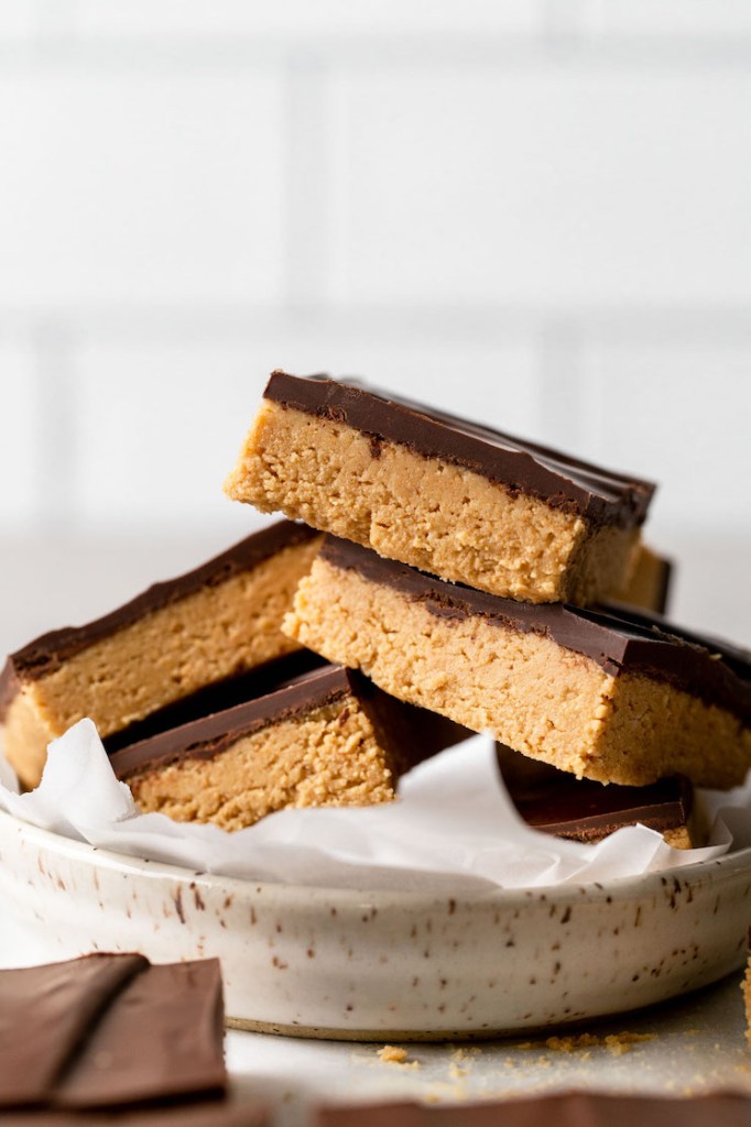 A pile of peanut butter chocolate bars in a speckled dish. More bars rest in the foreground. 