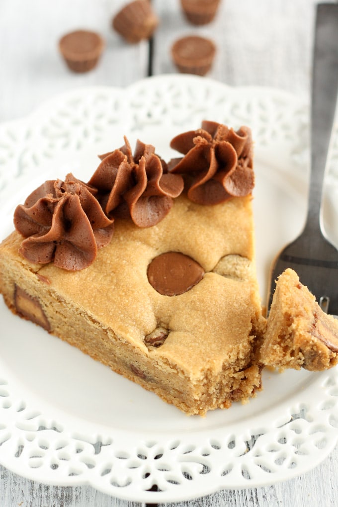 A slice of homemade cookie cake on a white plate with a fork. 