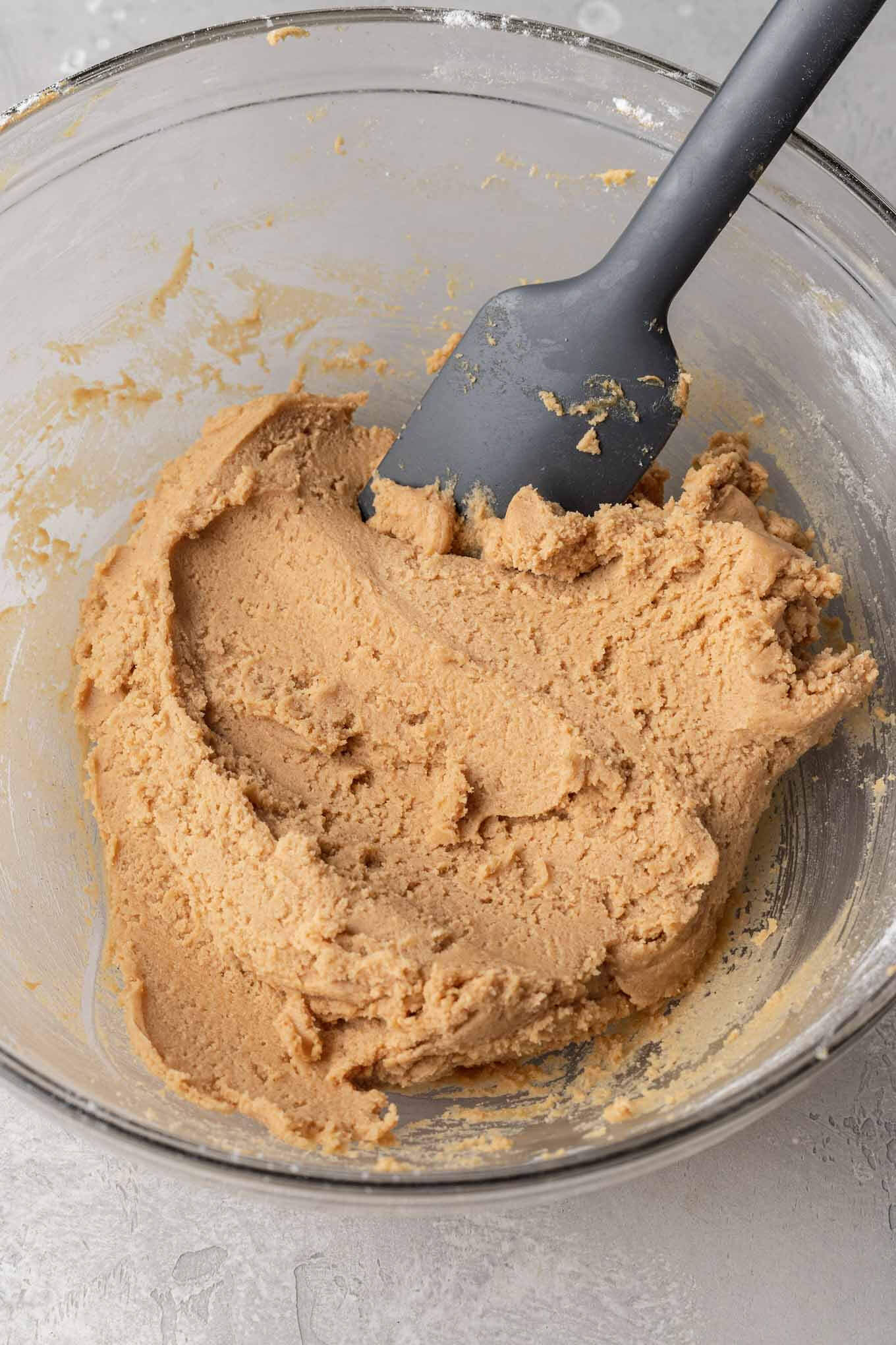 Peanut butter cookie dough in a glass mixing bowl, with a rubber spatula. 