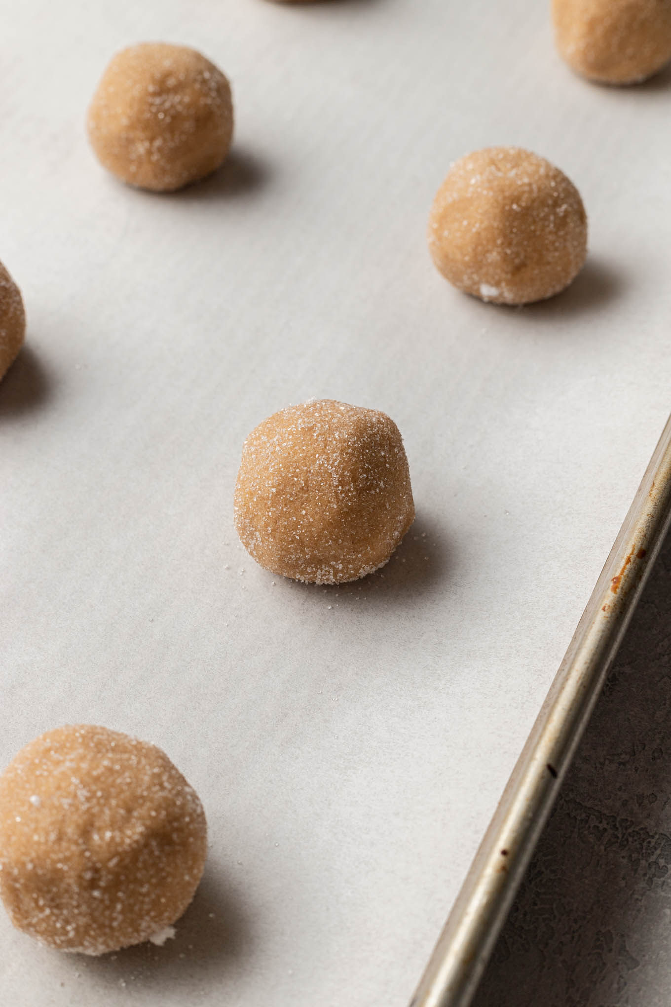 Peanut butter cookie dough balls on a parchment paper-lined baking sheet. 