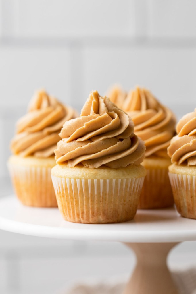 A marble cake stand holding several vanilla cupcakes topped with peanut butter frosting.