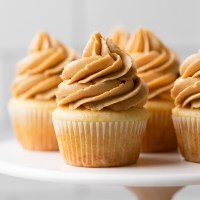 A marble cake stand holding several vanilla cupcakes topped with peanut butter frosting.