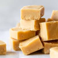 Pieces of Peanut Butter Fudge stacked on a gray surface and parchment paper.