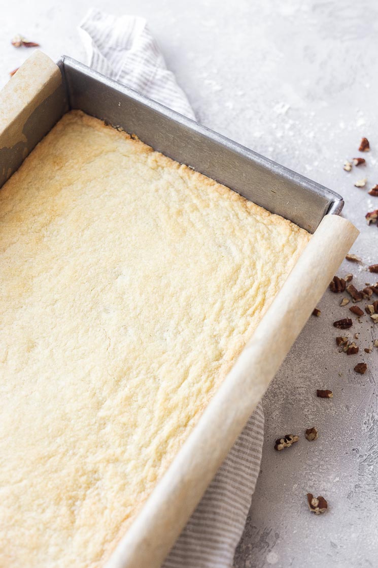 A baking pan lined with parchment paper and a baked shortbread crust.