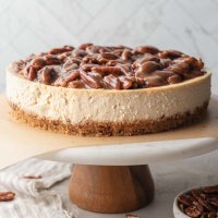 A pecan pie cheesecake sitting on top of a marble cake stand.