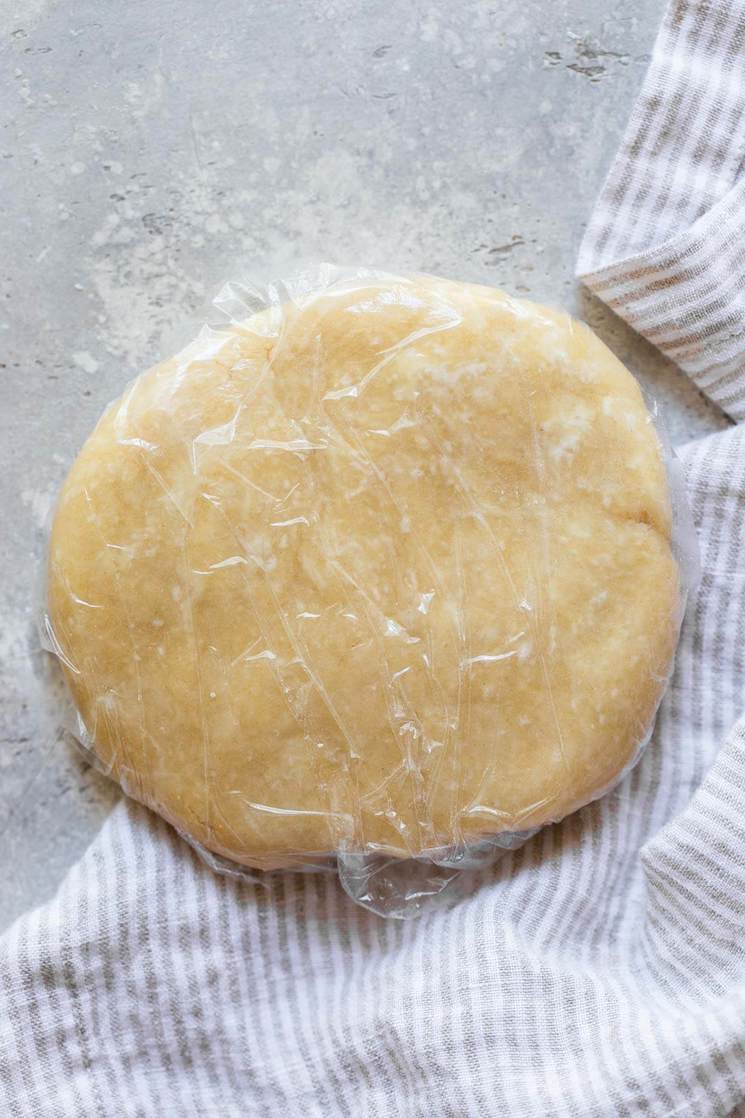 Homemade pie dough wrapped in plastic wrap sitting on top of a gray surface.