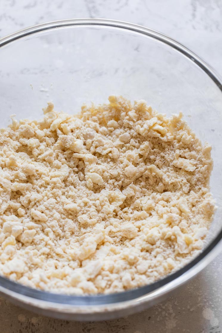 A glass bowl holding the dry ingredients with the butter cut into them.