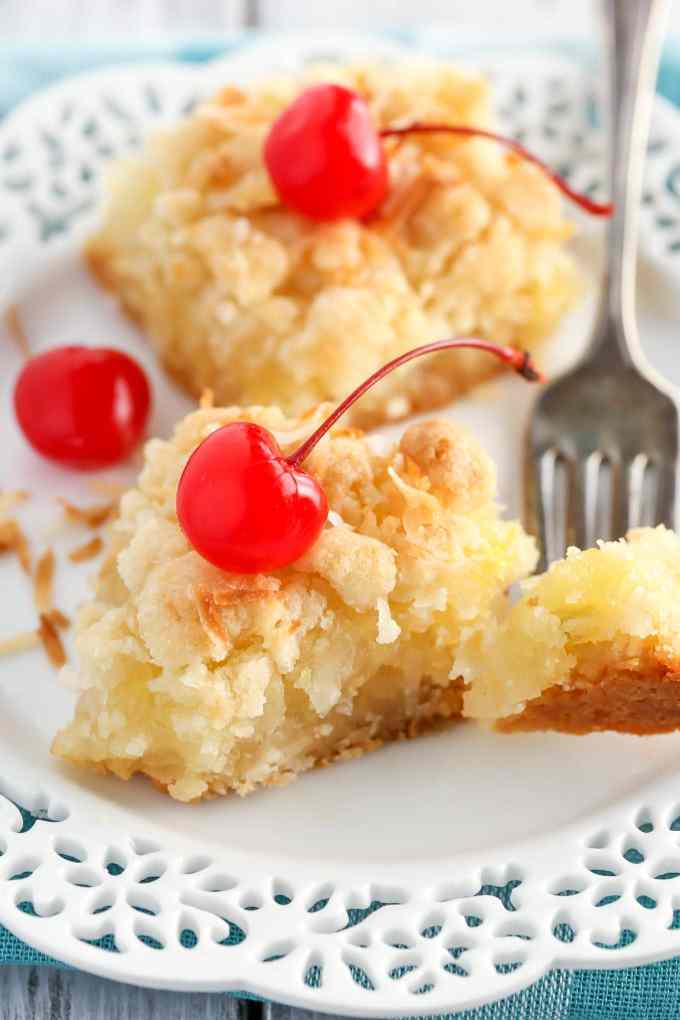 Two pineapple bars on a white dessert plate with a fork. A piece of the front bar is speared on the fork. 