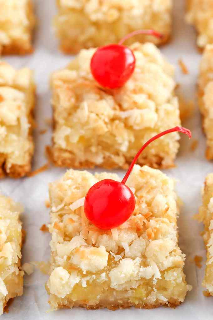 Three rows of sliced pineapple coconut bars. The front two have been garnished with maraschino cherries. 