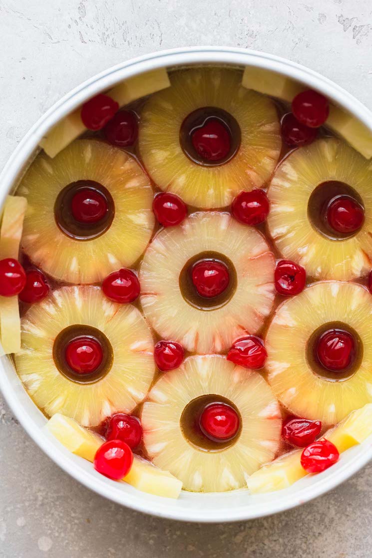 A round cake pan lined with pineapple slices, cherries, and the caramelized sugar topping.