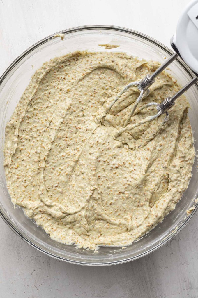 An overhead view of pistachio cake batter with electric beaters in a glass mixing bowl.