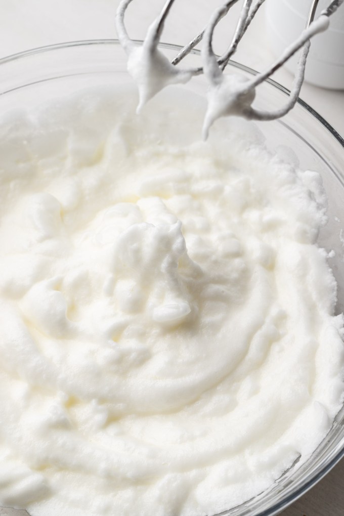 Whipped egg whites with electric beaters in a glass bowl.