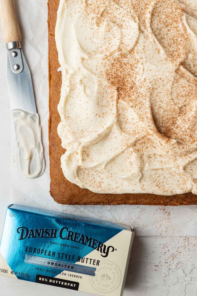 An overhead view of unsliced frosted pumpkin bars, with a spatula and a package of Danish Creamery butter. 