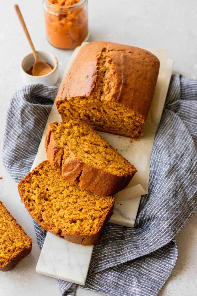 A loaf of pumpkin bread sliced and laying out on a marble serving tray.