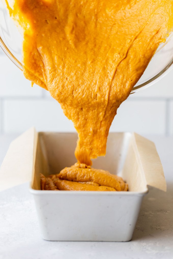 The batter being poured into a loaf pan lined with parchment paper.