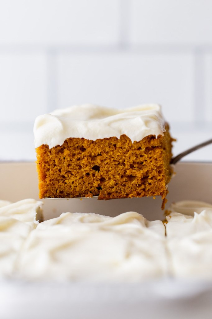 A single piece of cake being removed from the baking dish showing the cake and frosting layers.