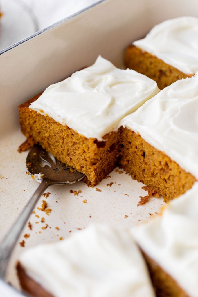 A baking dish holding a pumpkin cake with several pieces removed.