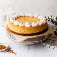 A pumpkin cheesecake on top of a cake stand with milk and cinnamon around it.