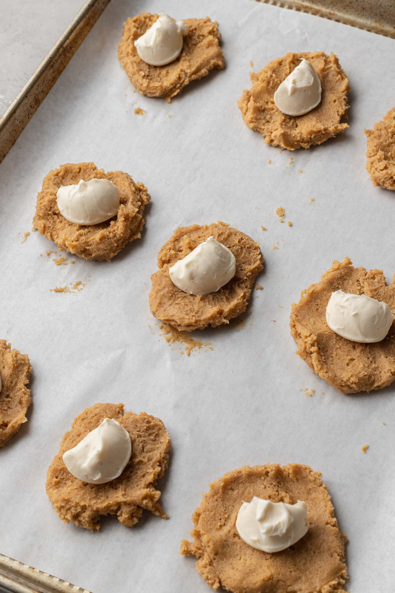 An overhead view of flattened balls of cookie dough with scoops of cream cheese in the center. 