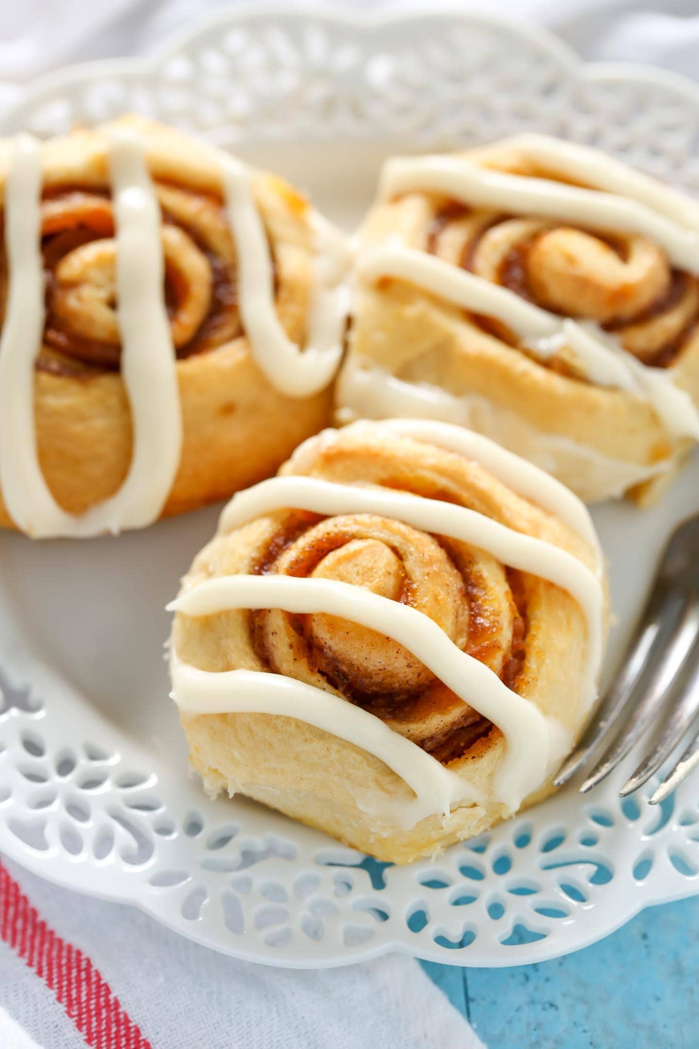 Three iced pumpkin cinnamon rolls on a white plate.