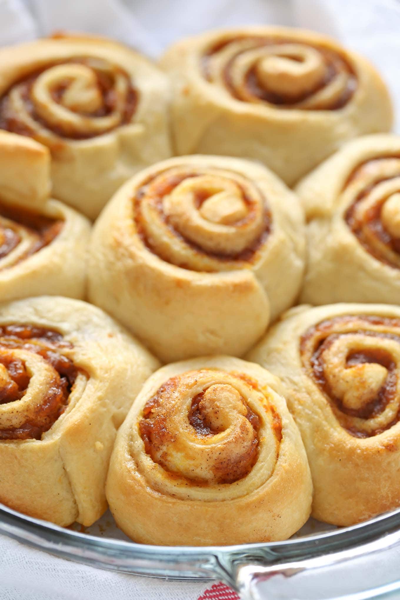 A pie plate of baked pumpkin spice cinnamon rolls waiting to be iced. 