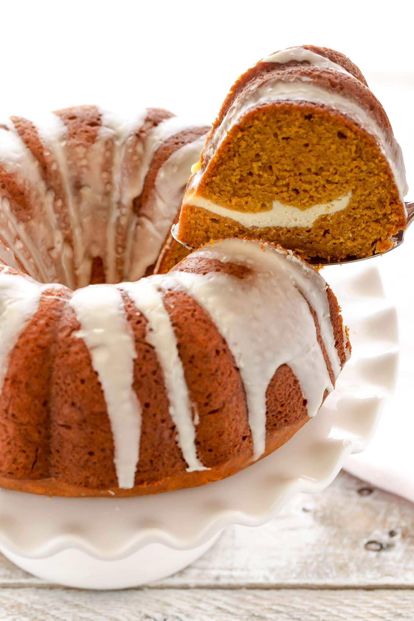 A slice of pumpkin spice bundt cake being removed from a cake stand. 