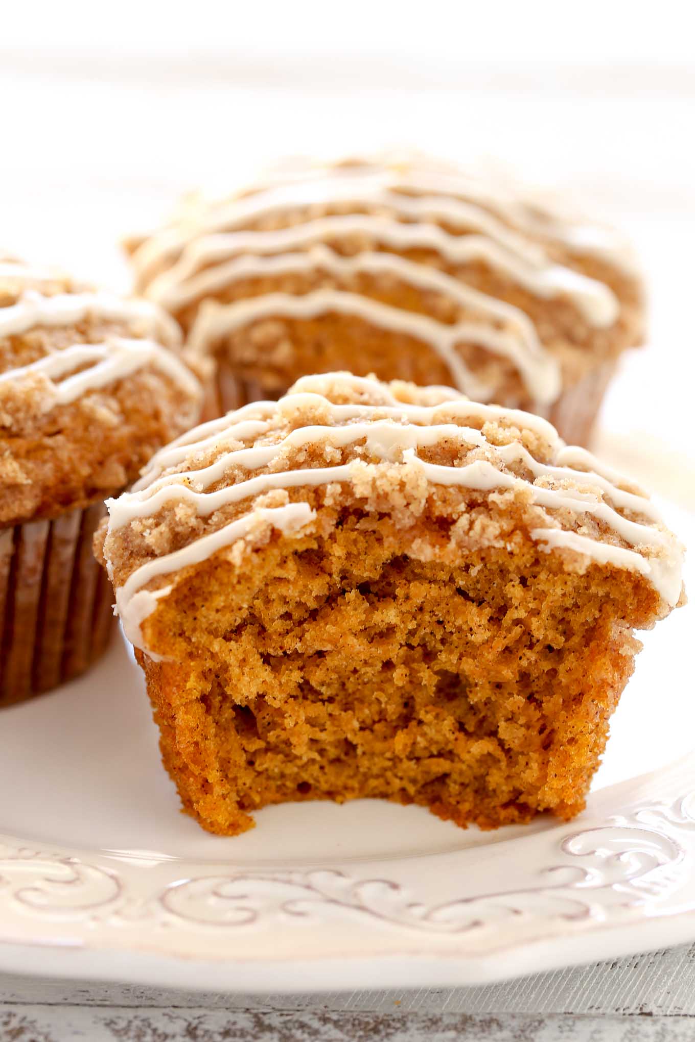 Close up view of pumpkin muffins on a white plate. The front muffin has a bite missing. 