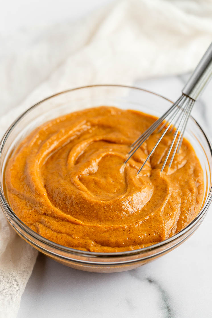 A glass bowl filled with pumpkin cupcake batter and a metal whisk.