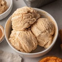 An overhead view of a white bowl with three scoops of pumpkin ice cream.