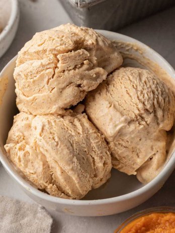 An overhead view of a white bowl with three scoops of pumpkin ice cream.