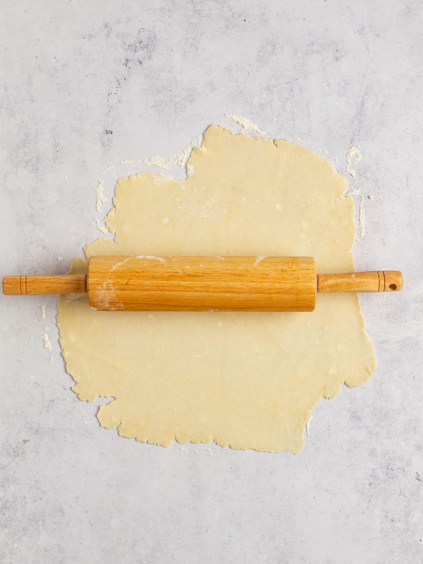 Pie dough rolled out on a gray surface.