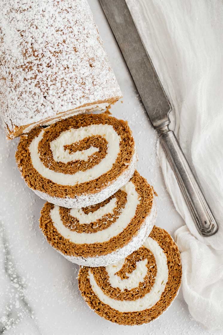 A partially sliced pumpkin roll on a marble surface.