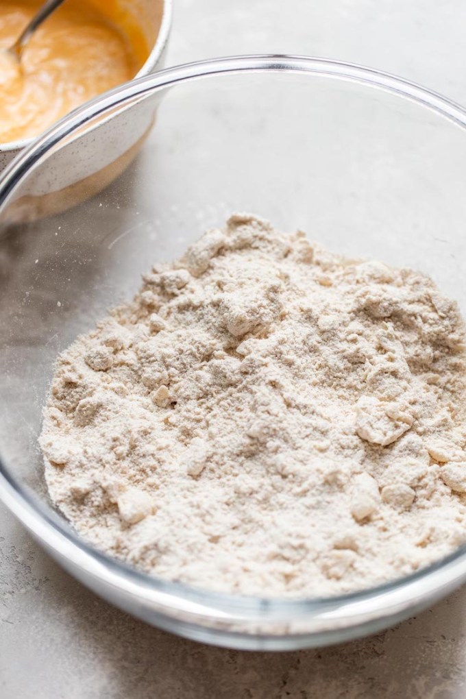 The dry ingredients for scones in a glass mixing bowl and cold butter cut into it.