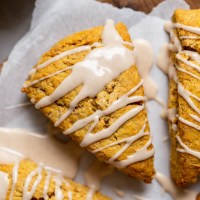 A pumpkin scone topped with maple cinnamon glaze on a piece of parchment paper.