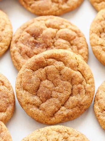 Several pumpkin cookies lined up on a piece of parchment paper.