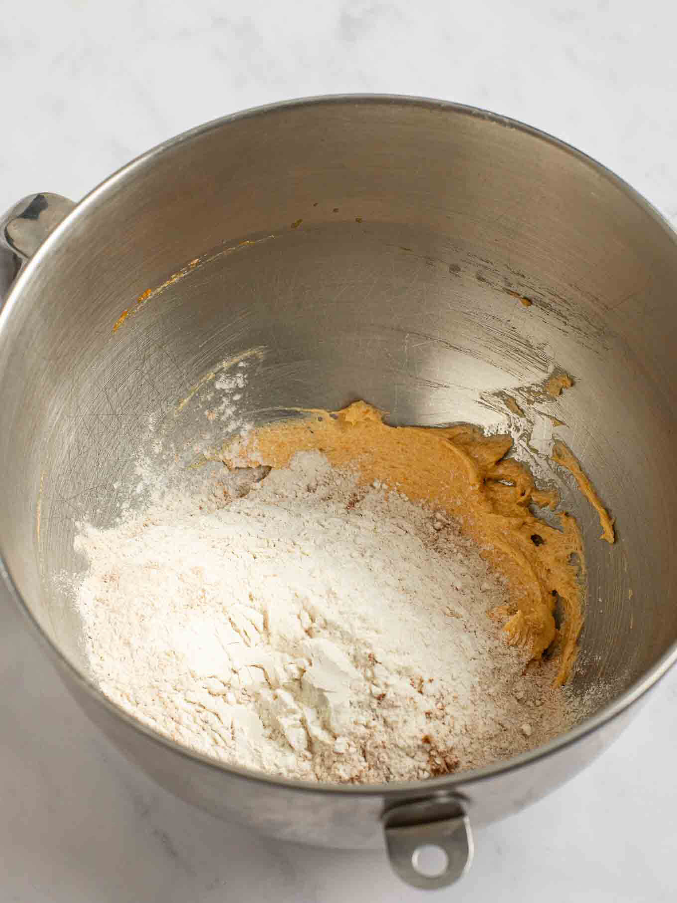 The dry ingredients added on top of the wet ingredients in the bowl of a stand mixer.