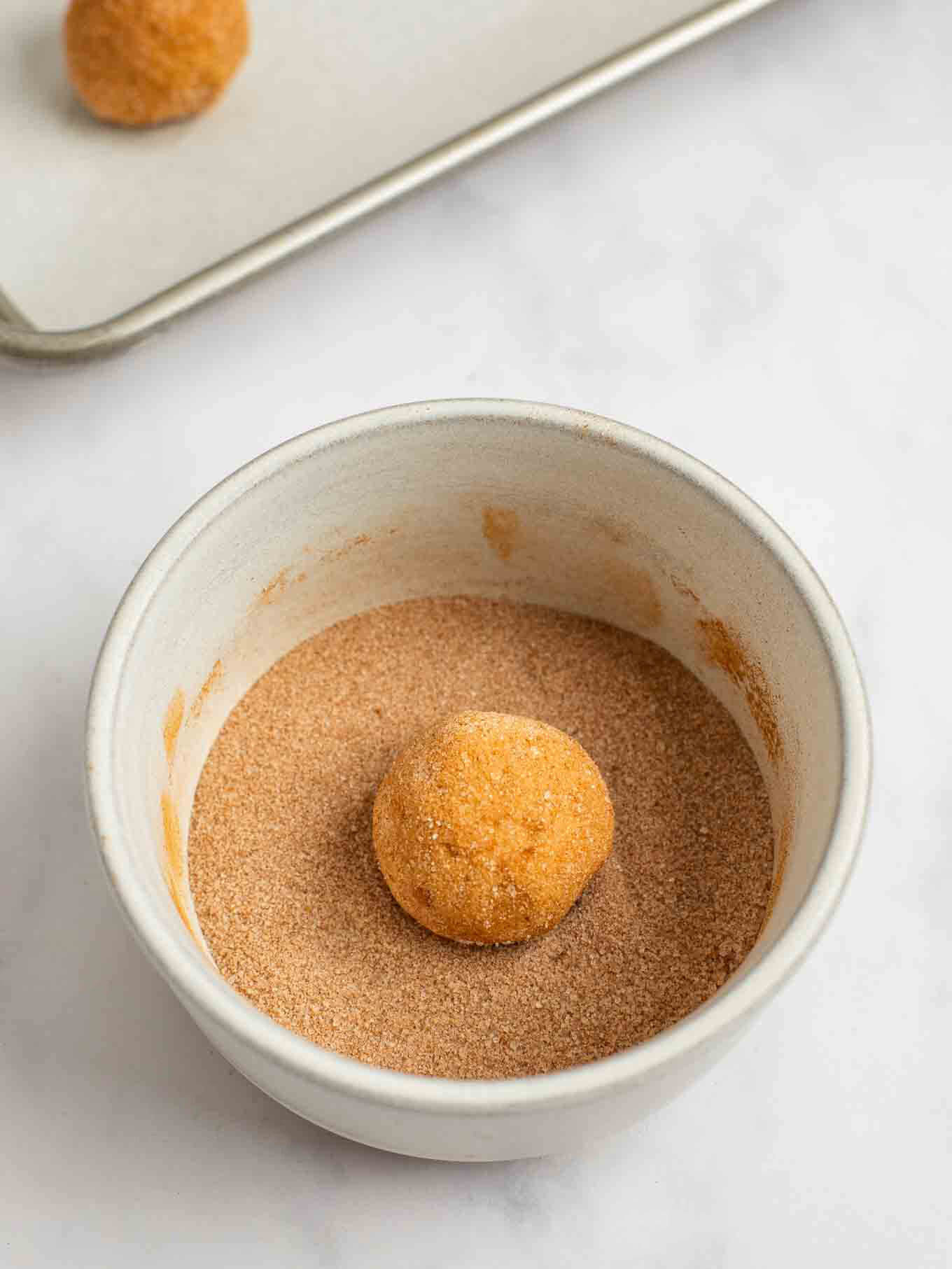 A ball of cookie dough being rolled in cinnamon and sugar.