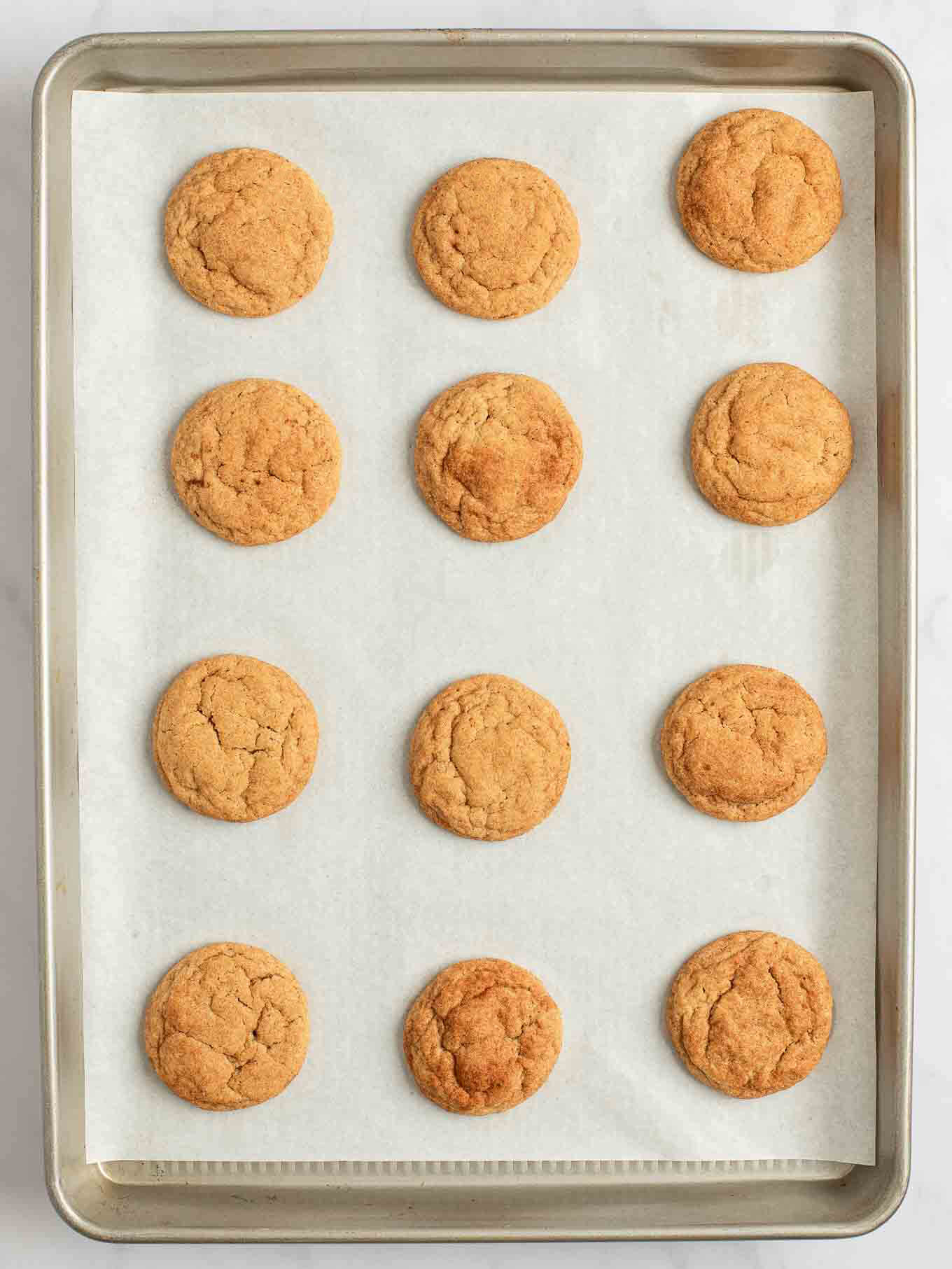 An overhead view of pumpkin snickerdoodles fully baked on a baking sheet.