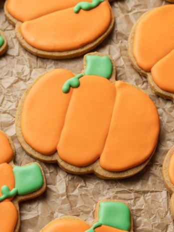 Several iced pumpkin sugar cookies on a piece of parchment paper.