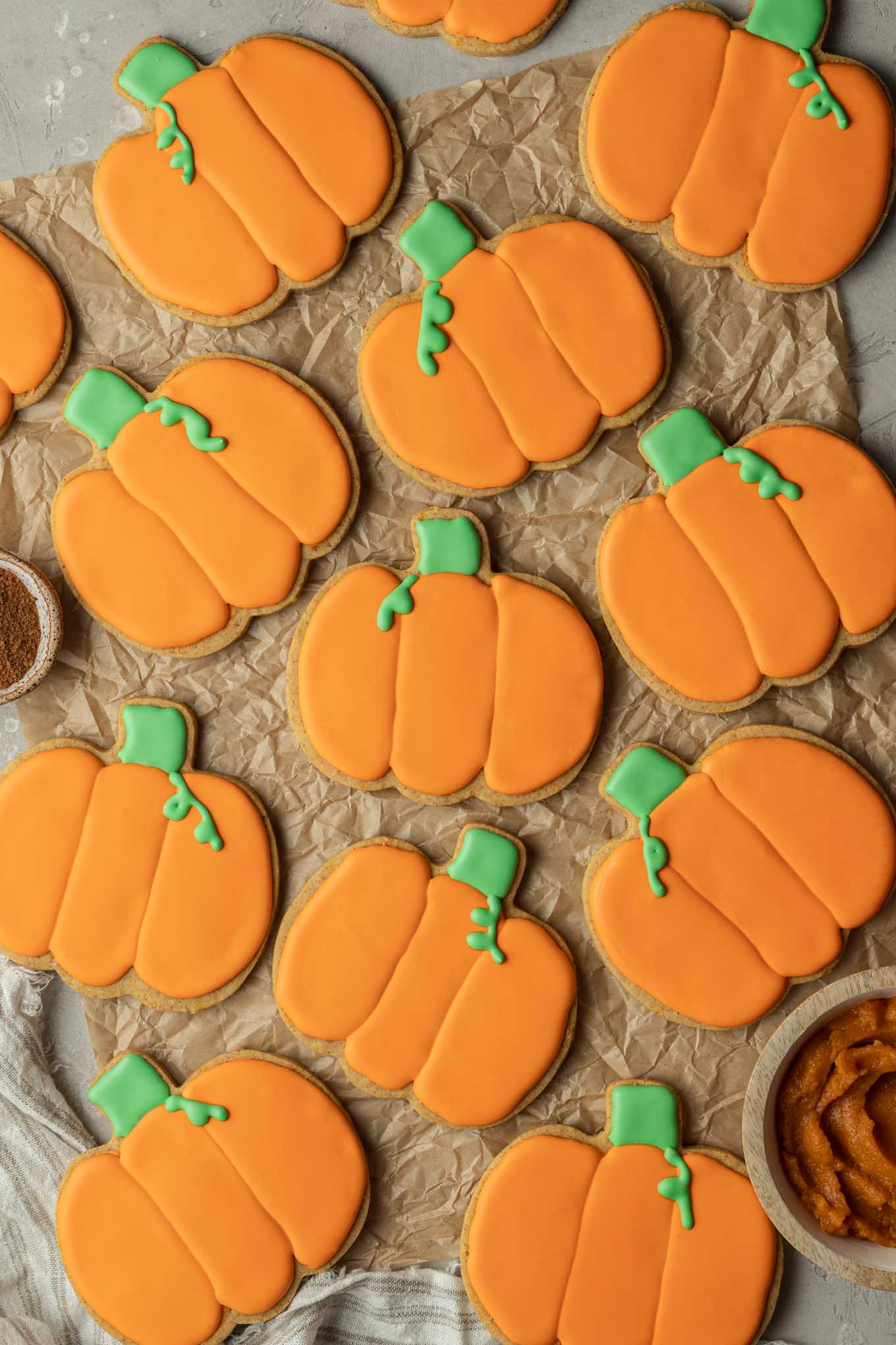 An overhead view of decorated pumpkin cookies on parchment paper. 