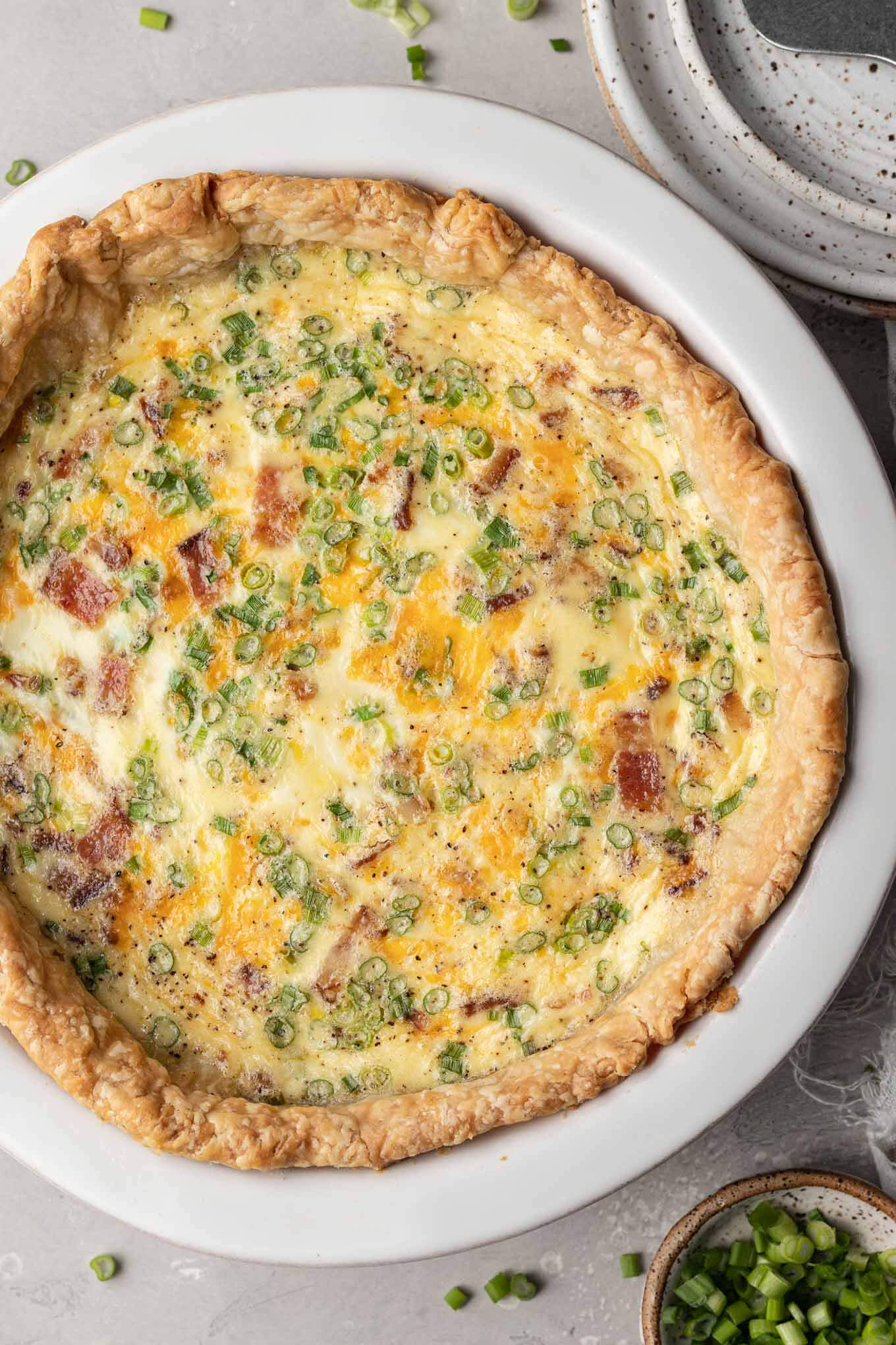 An overhead view of a baked bacon and cheese quiche in a white pie plate. 