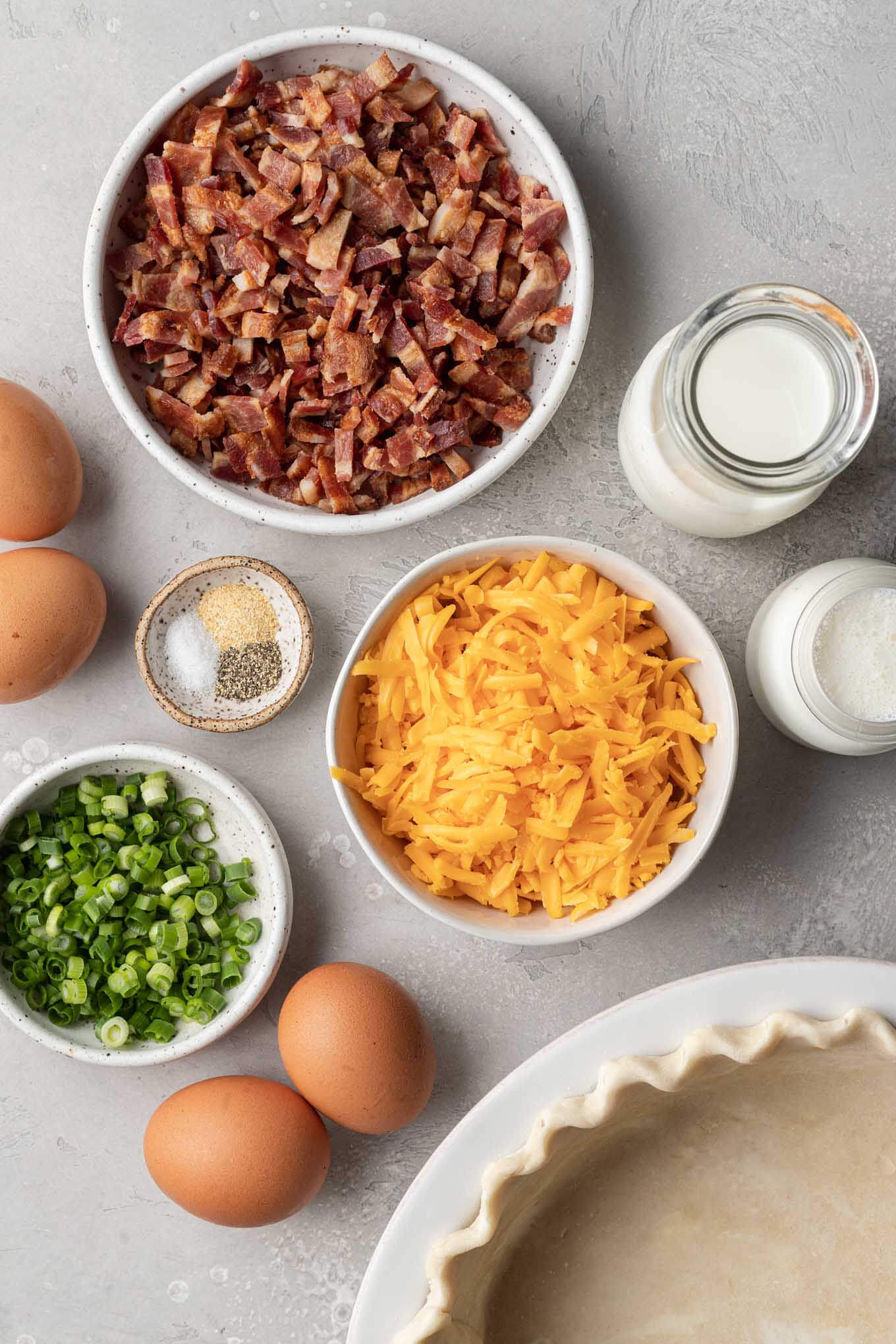 An overhead view of the ingredients needed to make bacon and cheddar quiche. 