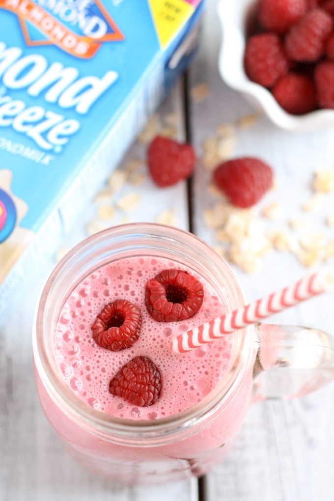 Overhead view of a raspberry almond milk smoothie next to a carton of almond milk and a bowl of fresh berries. 