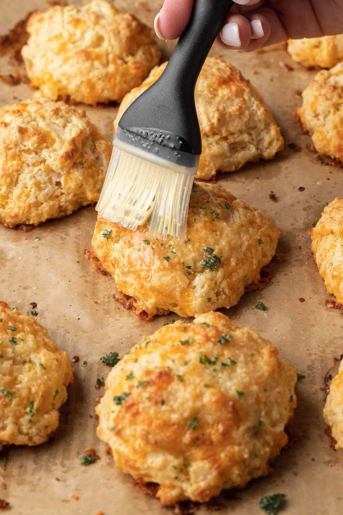 Red Lobster cheddar biscuits on parchment paper being brushed with a buttery topping.