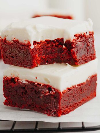 Two red velvet brownies stacked on top of each other. The top brownie has a bite missing.