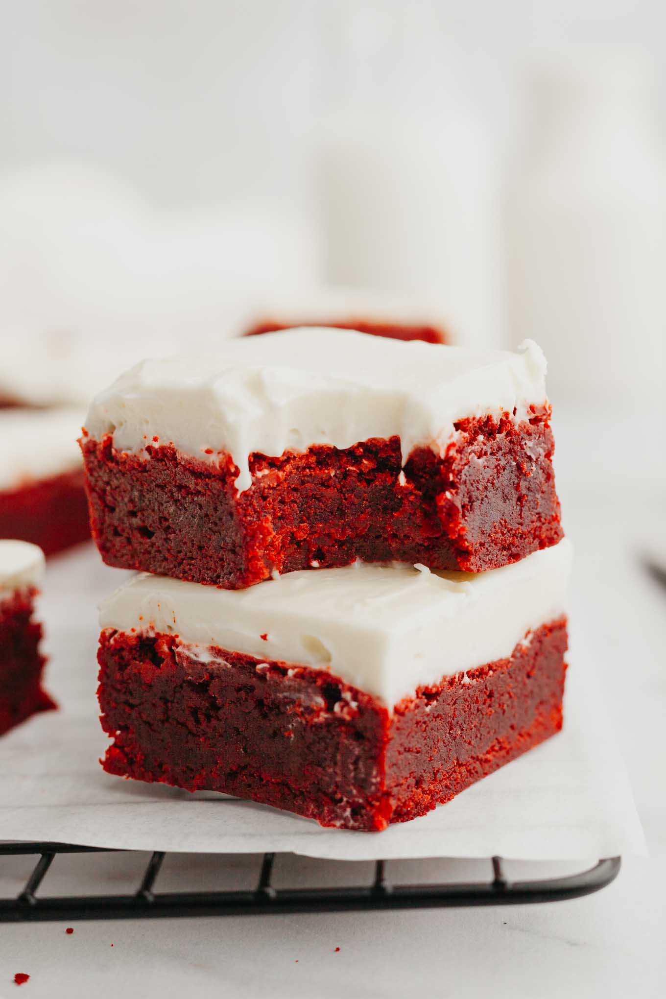 Two red velvet brownies stacked on top of each other; the top one has a bite missing. 