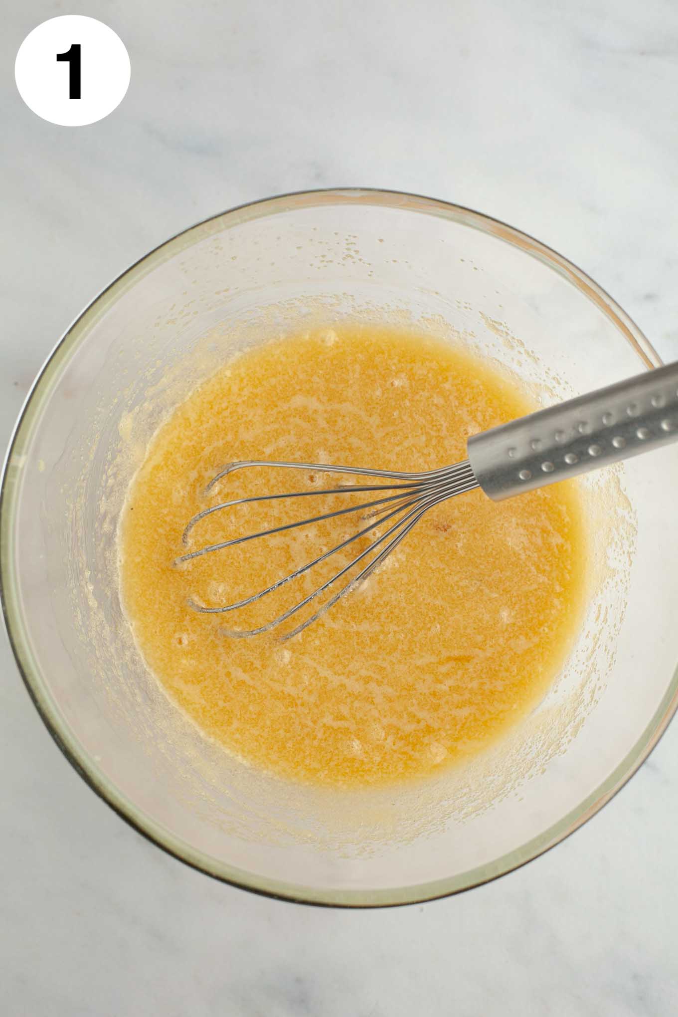 Melted butter and sugar whisked together in a glass mixing bowl.