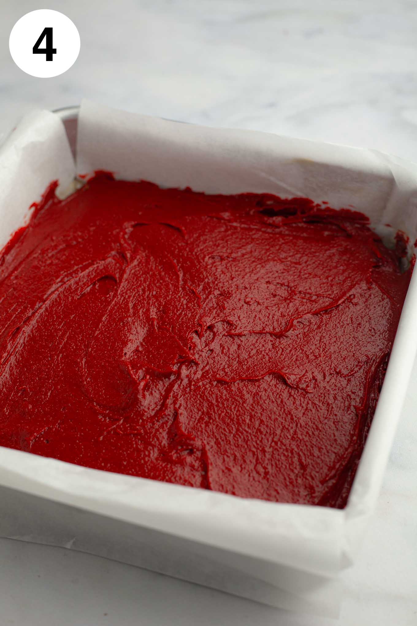 Red velvet brownie batter smoothed out into a parchment paper lined baking pan.