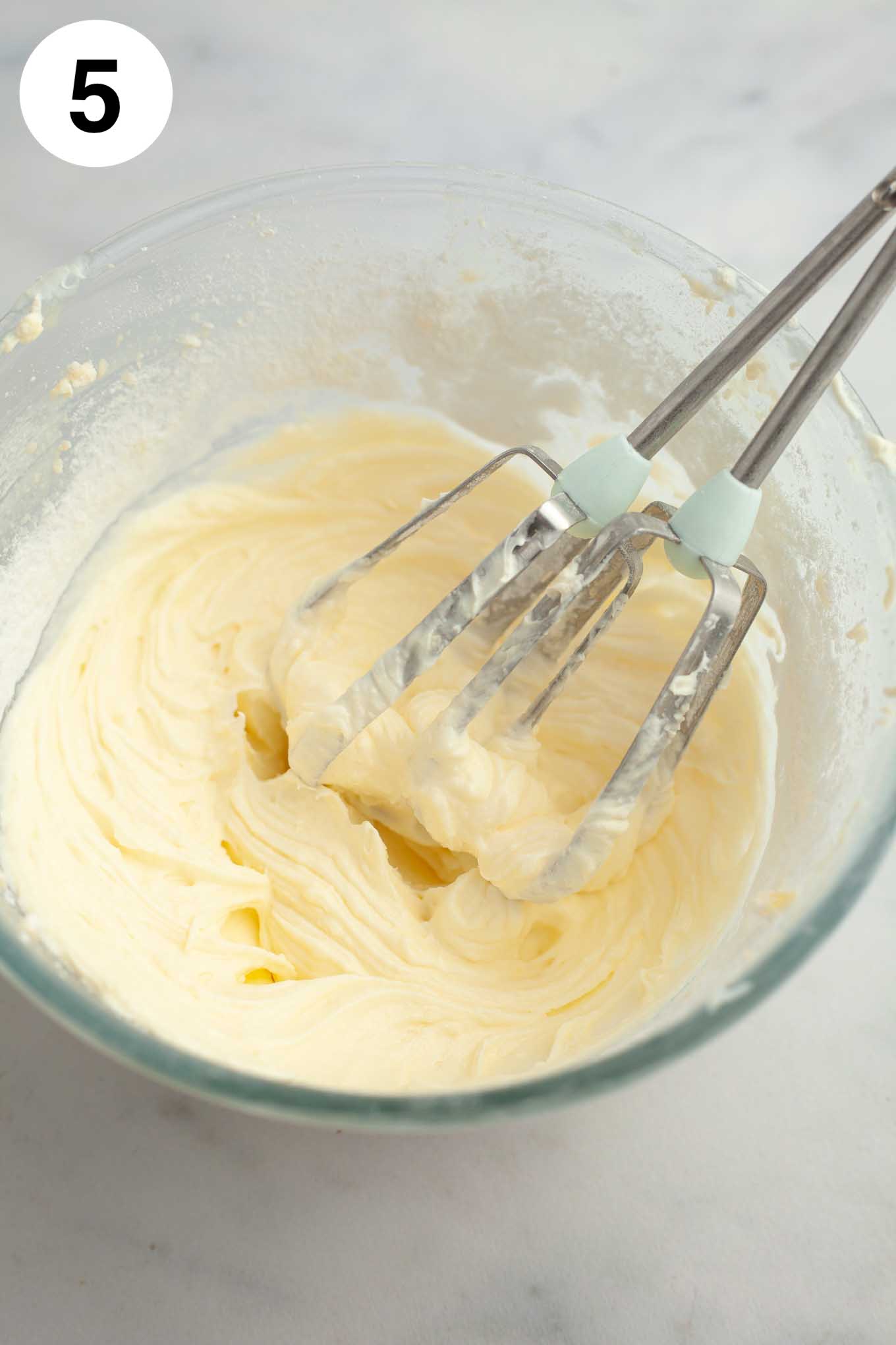 Cream cheese icing mixed together in a glass mixing bowl.